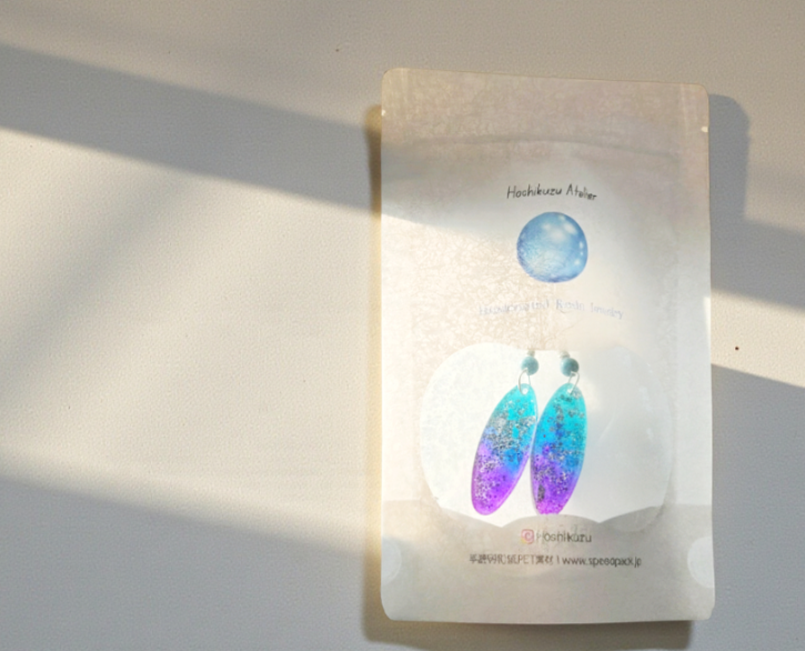 透明感のあるデザインが特徴のオリジナルビニールパウチ。青と紫のグラデーションピアスを際立たせるパッケージデザイン印刷と小ロットパッケージ印刷の事例。